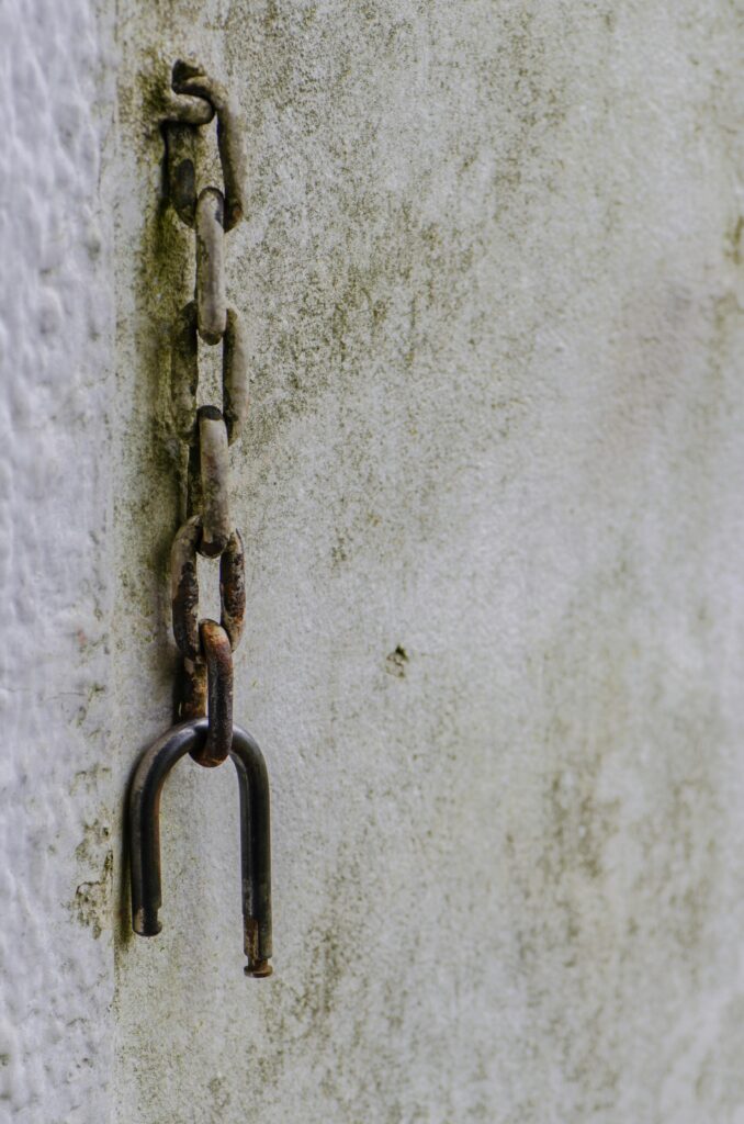 Old rusty chain hanging against a textured and weathered wall surface, evoking an industrial feel.