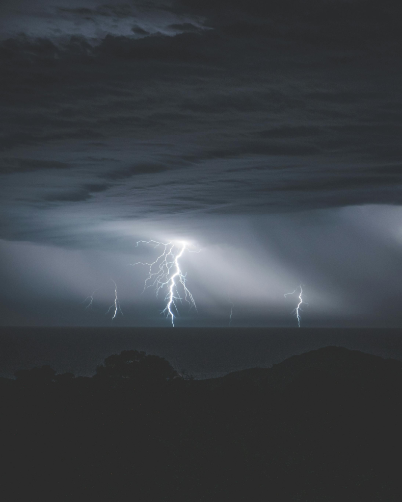 Shiny dangerous majestic lightnings with thunder in cloudy sky over water of ocean at night