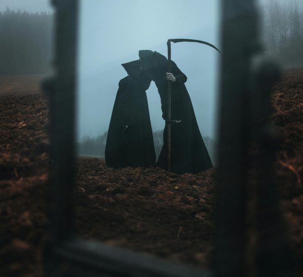 Eerie figure with a scythe, reflected in a mirror on a foggy landscape.